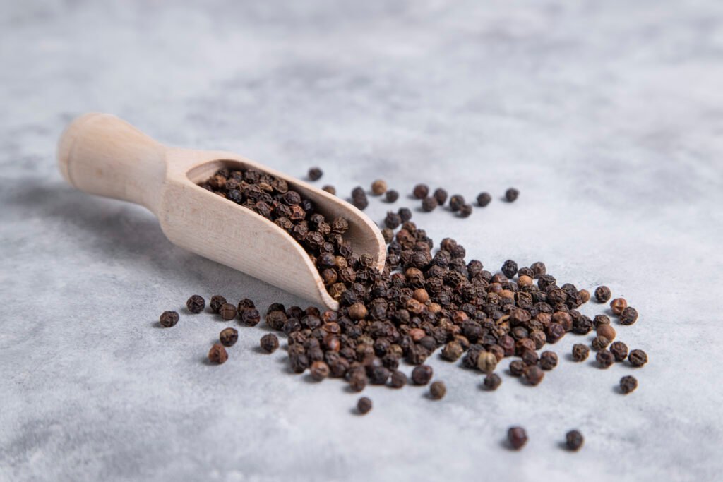 A wooden spoon full of black pepper corns placed on stone table . High quality photo